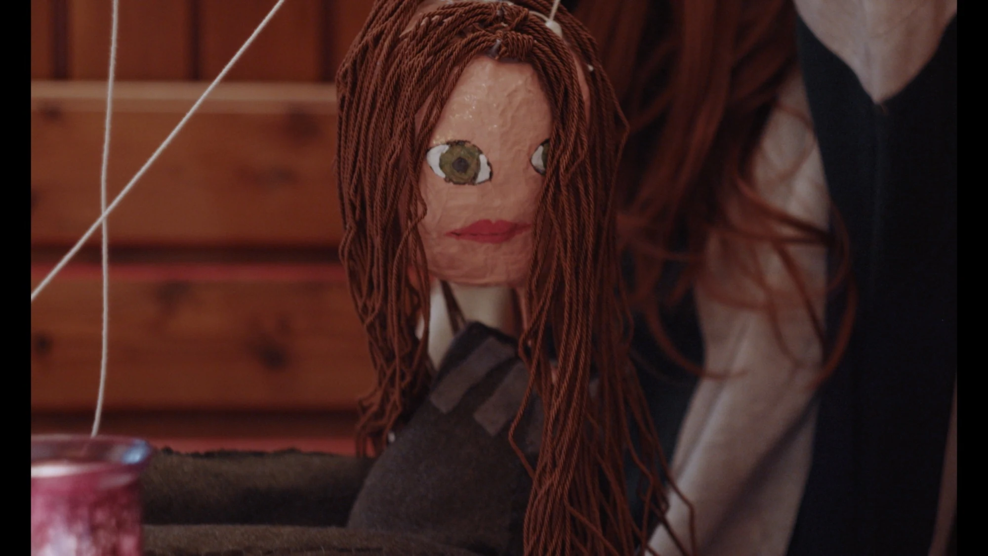 A close-up of a handmade puppet with long red hair.